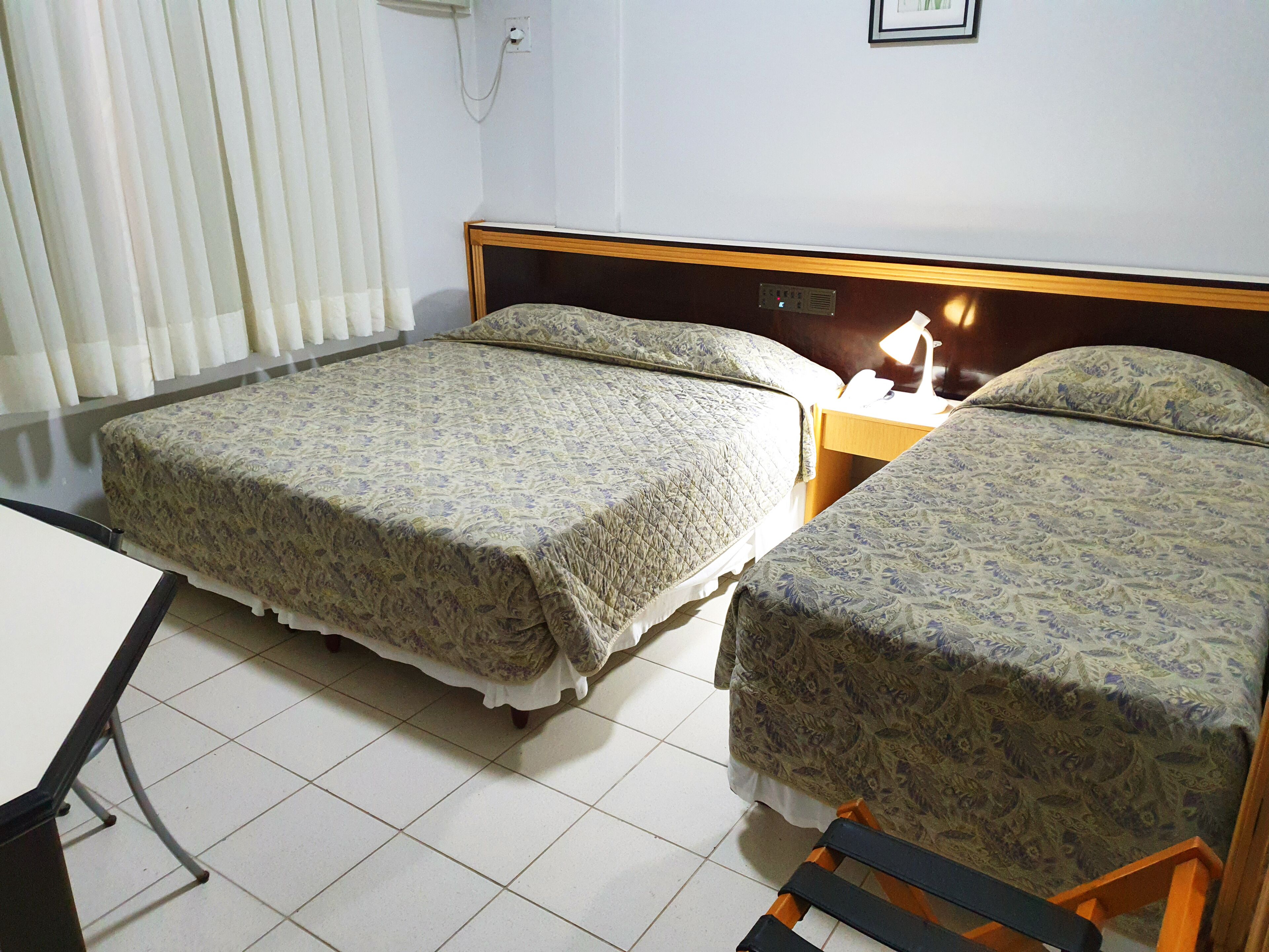 Une chambre d’hôtel avec deux lits, une table de chevet et une fenêtre avec des rideaux.