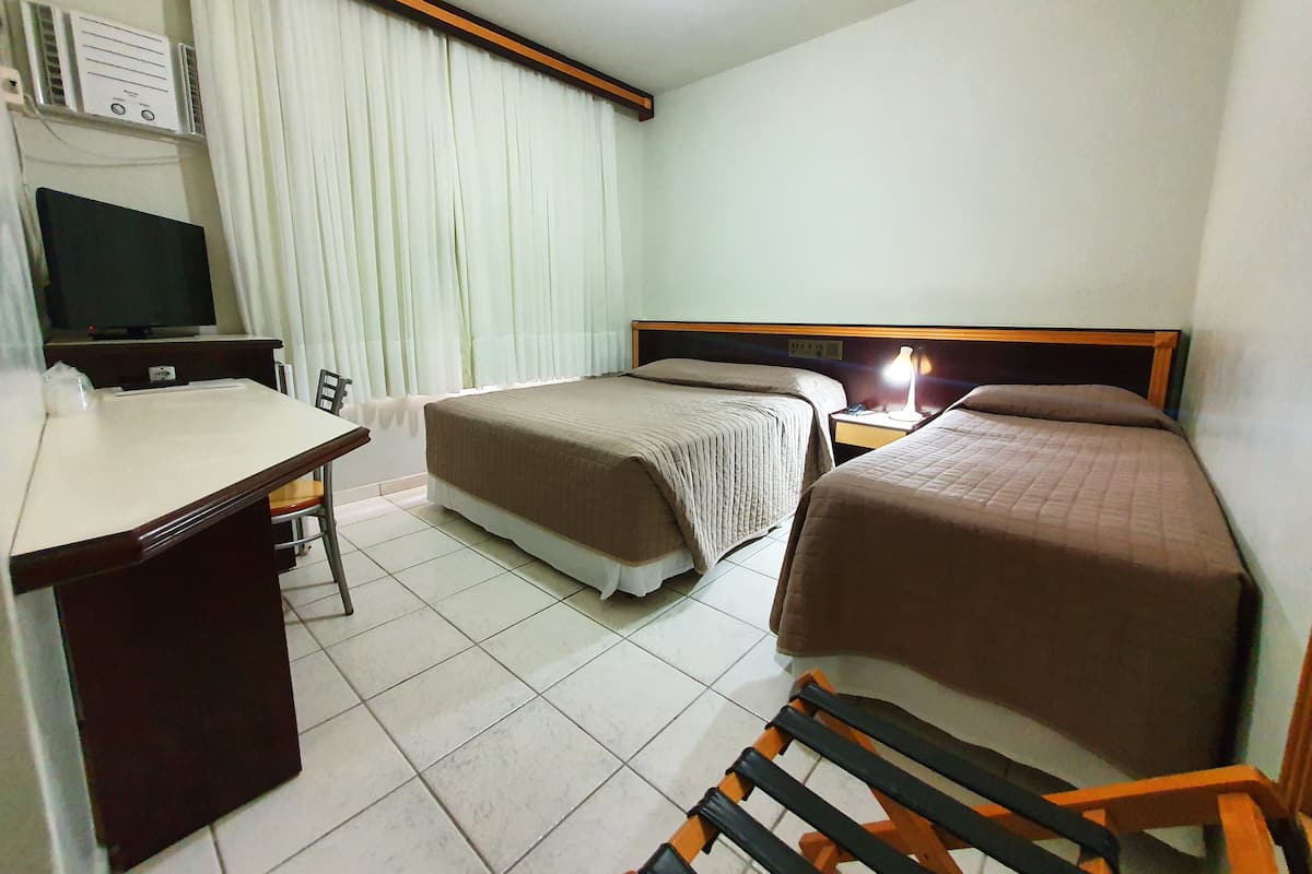 A hotel room with two beds, a desk, a chair, a TV, and a lamp.