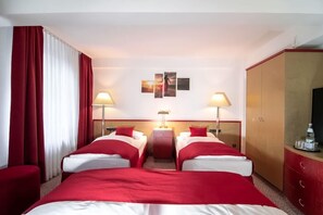 Une chambre d’hôtel avec deux lits, une literie rouge, une table de chevet avec des lampes, une armoire et une œuvre d’art accrochée au mur.