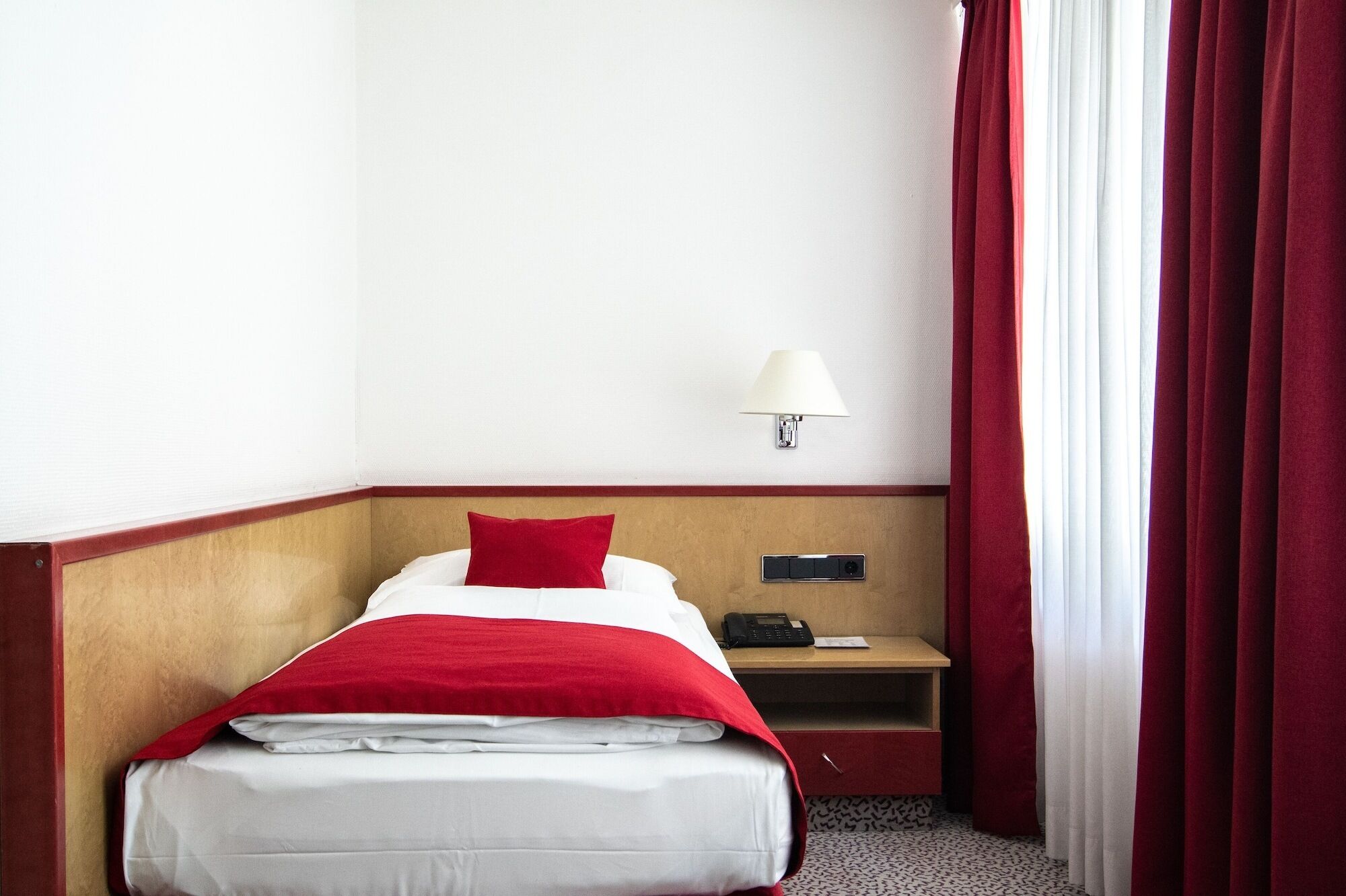 A hotel room with a bed, a nightstand, a lamp, and a telephone.