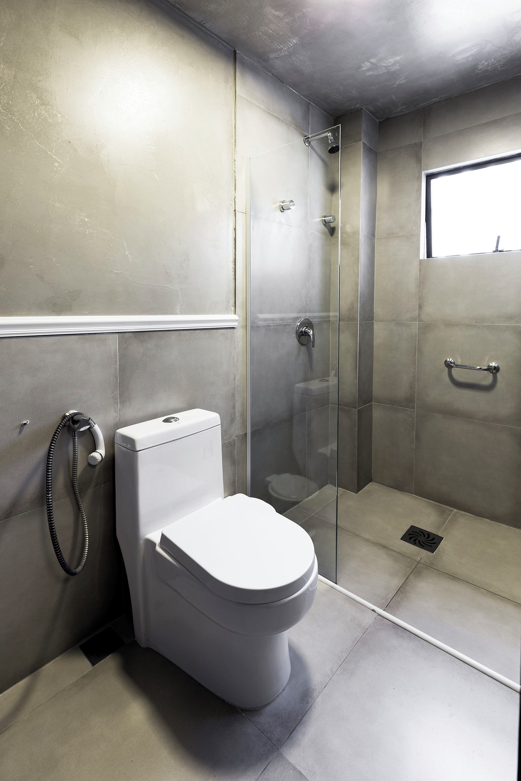 Une salle de bain moderne équipée de toilettes, d’une douche avec une porte en verre et d’une fenêtre laissant entrer la lumière naturelle.