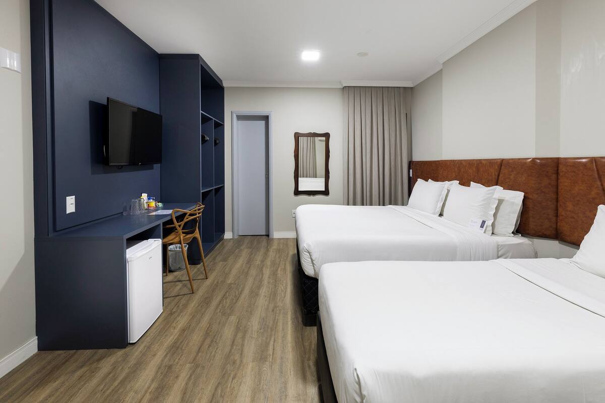 Une chambre d’hôtel avec deux lits, un bureau avec une télévision, un petit réfrigérateur et un miroir.