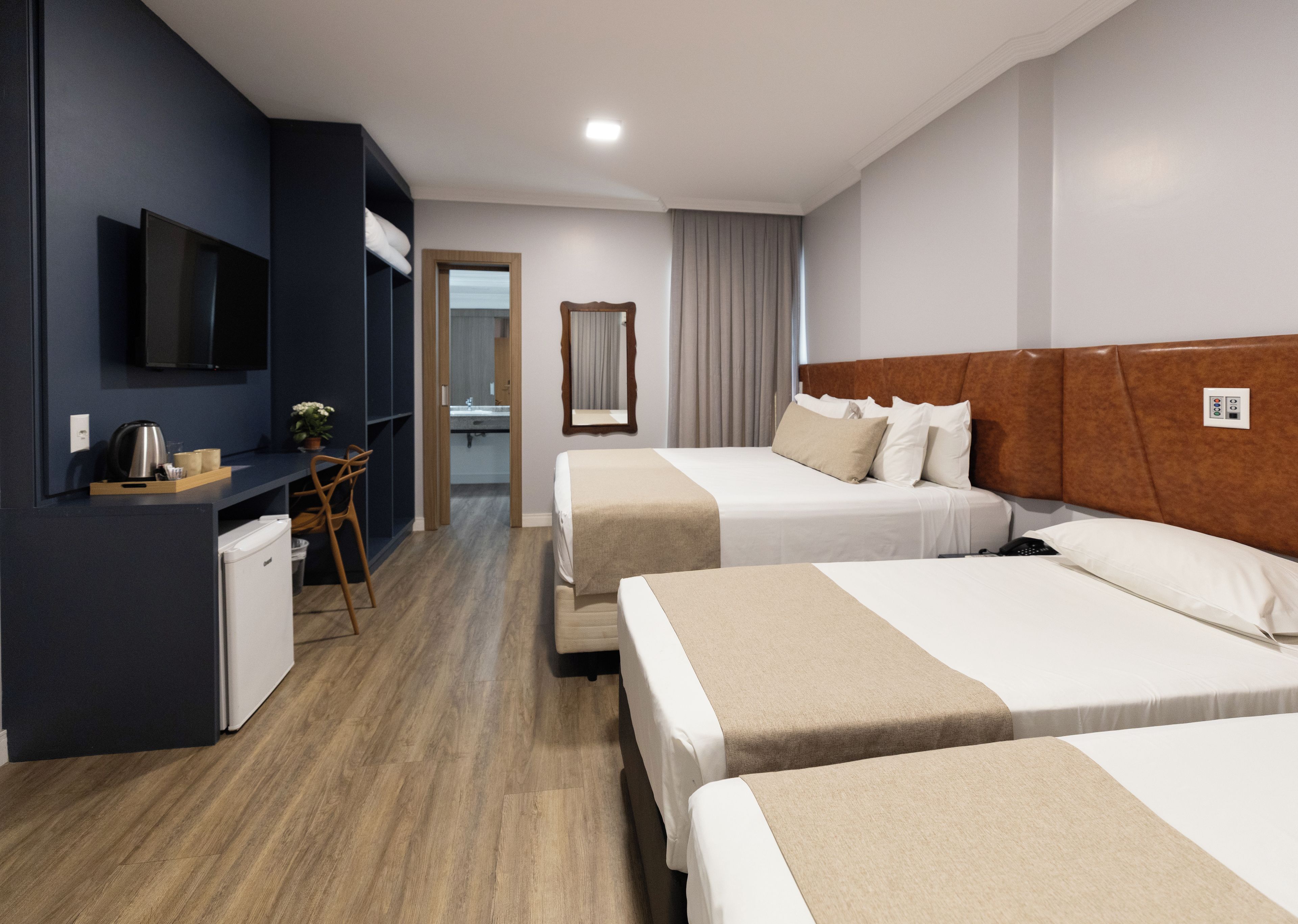 A hotel room with two beds, a desk with a chair, a television, and a small kitchenette.