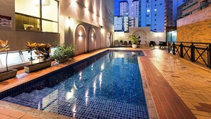Una piscina con suelo de baldosas, plantas en macetas y mobiliario exterior.