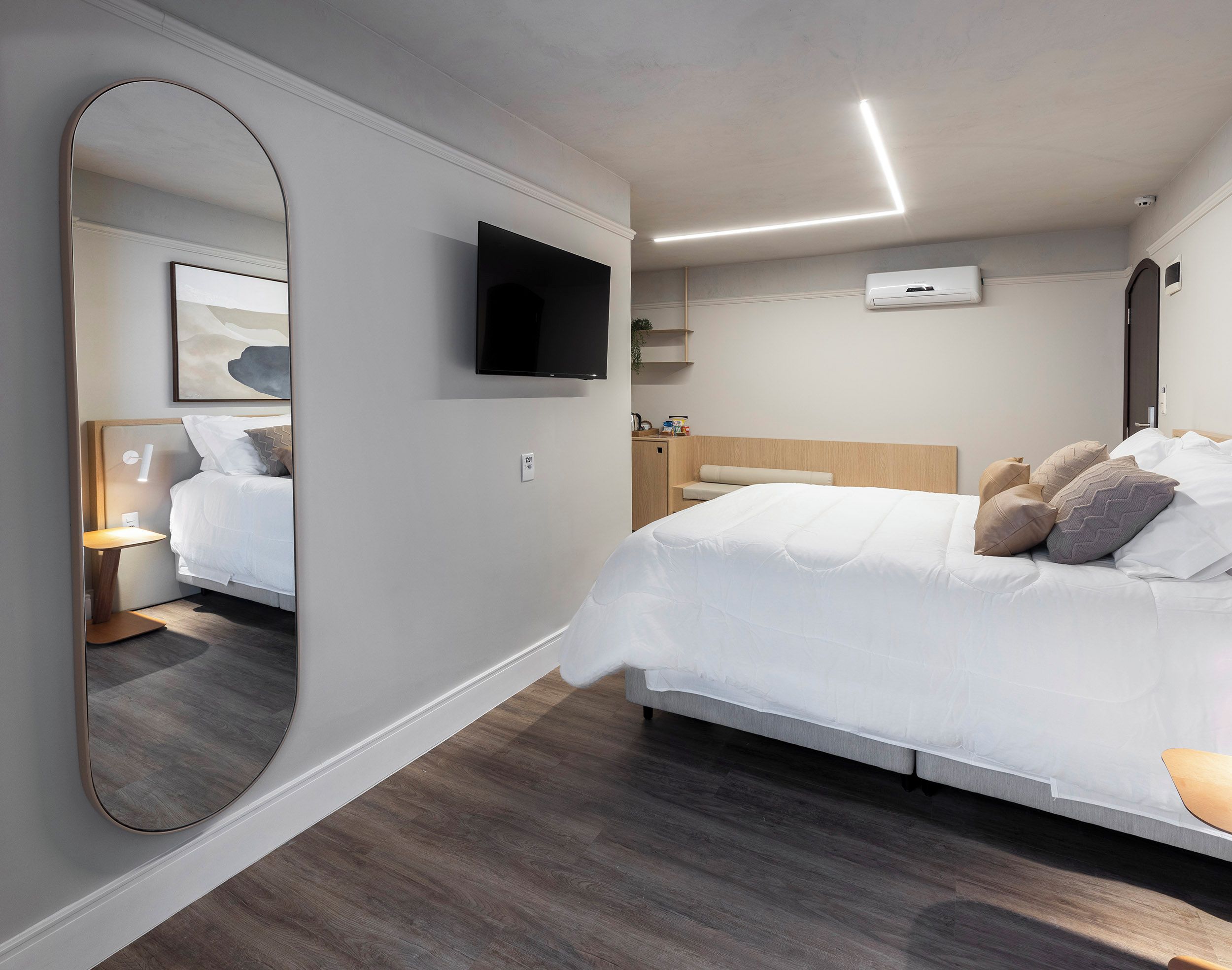 Een moderne hotelkamer met een groot bed, een aan de muur bevestigde televisie, een nachtkastje met een lamp en een grote spiegel.