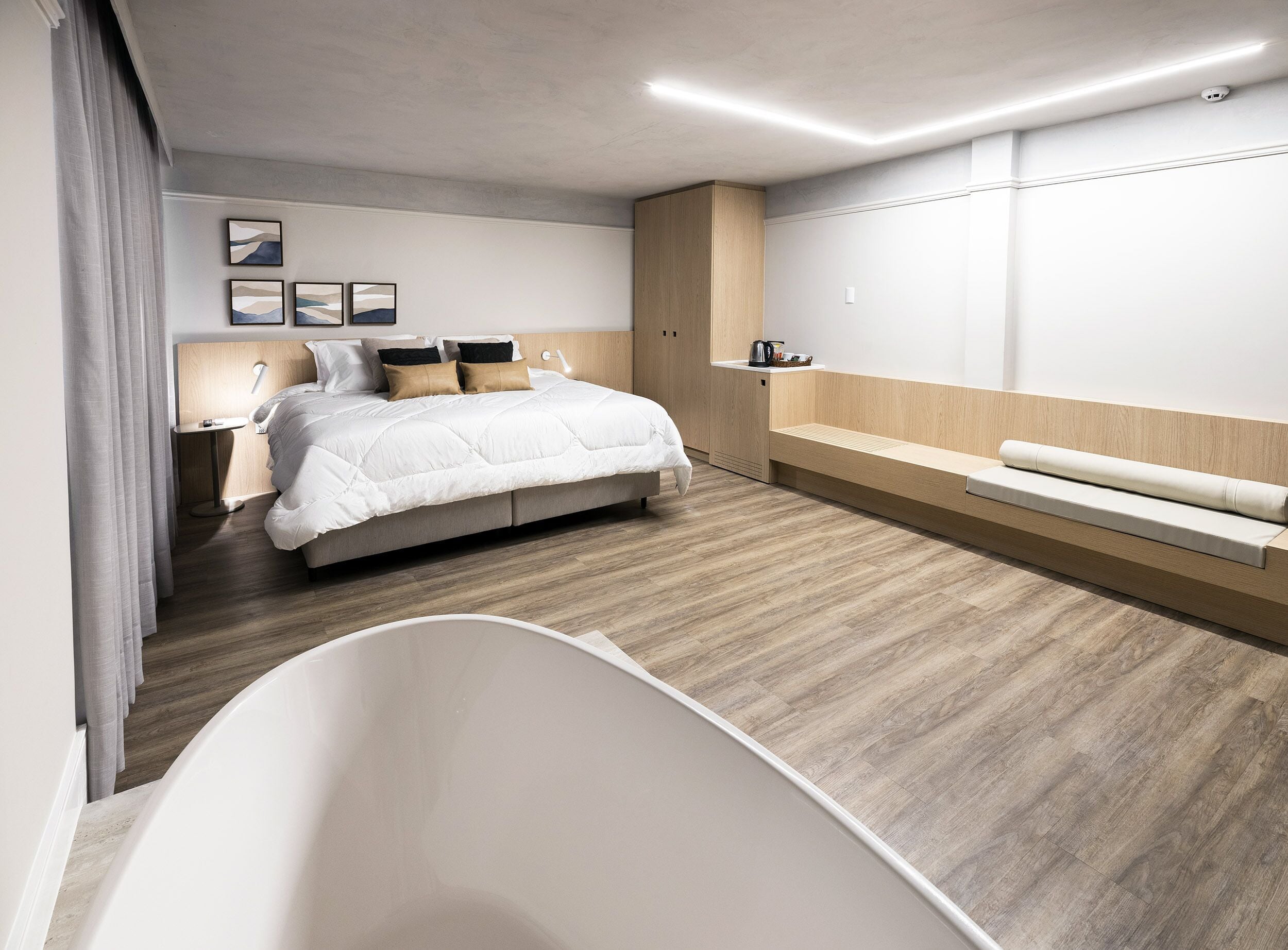 Un dormitorio moderno con una cama grande, mesitas de noche, un banco y una bañera.