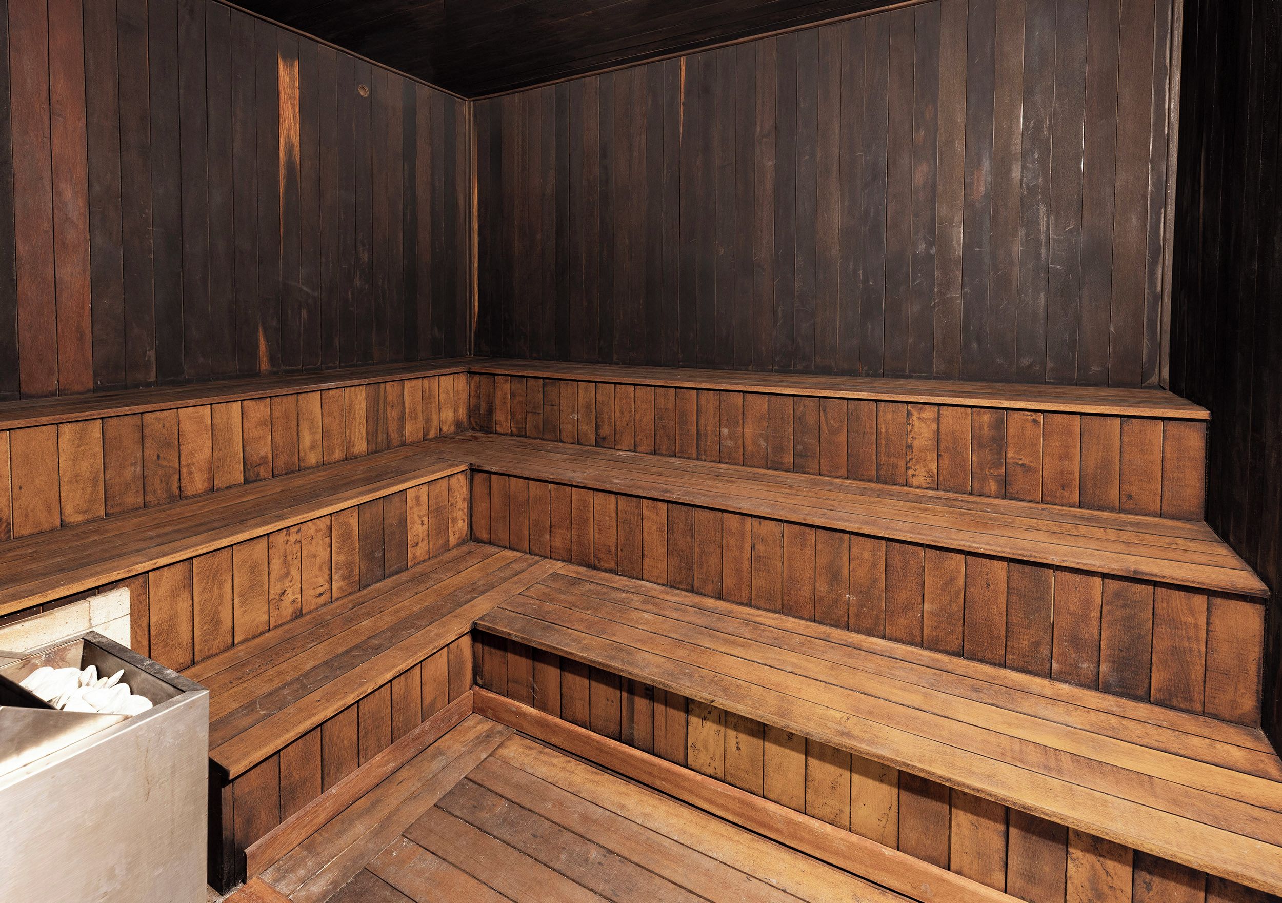 A sauna with wooden benches and a metal container.