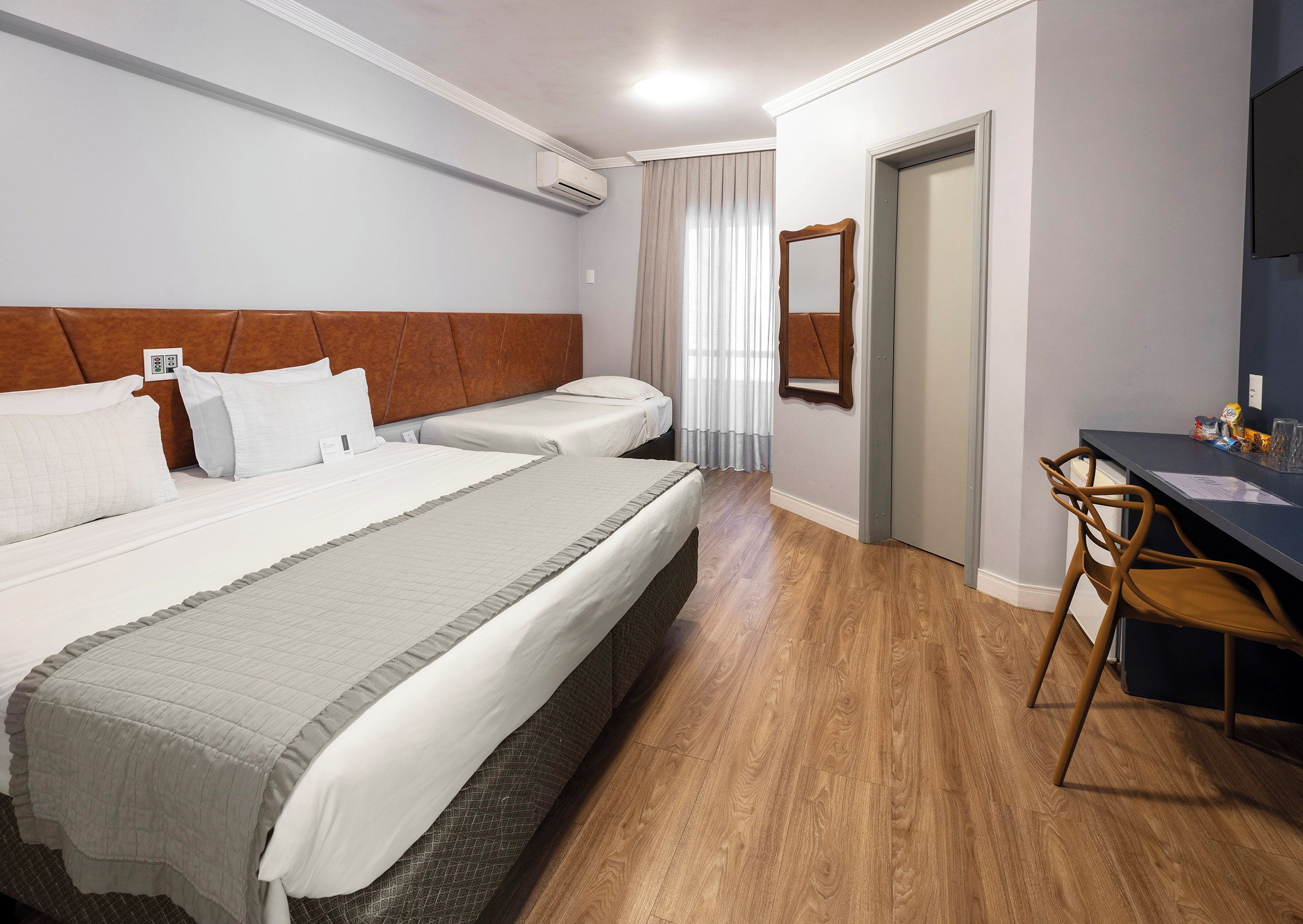 Habitación de hotel con dos camas, un escritorio, una silla, un espejo y una puerta.