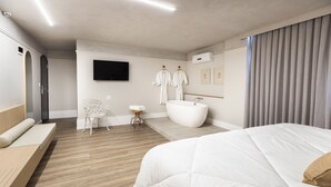 Una habitación de hotel moderna con una cama grande, una bañera, un televisor de pantalla plana y una silla.