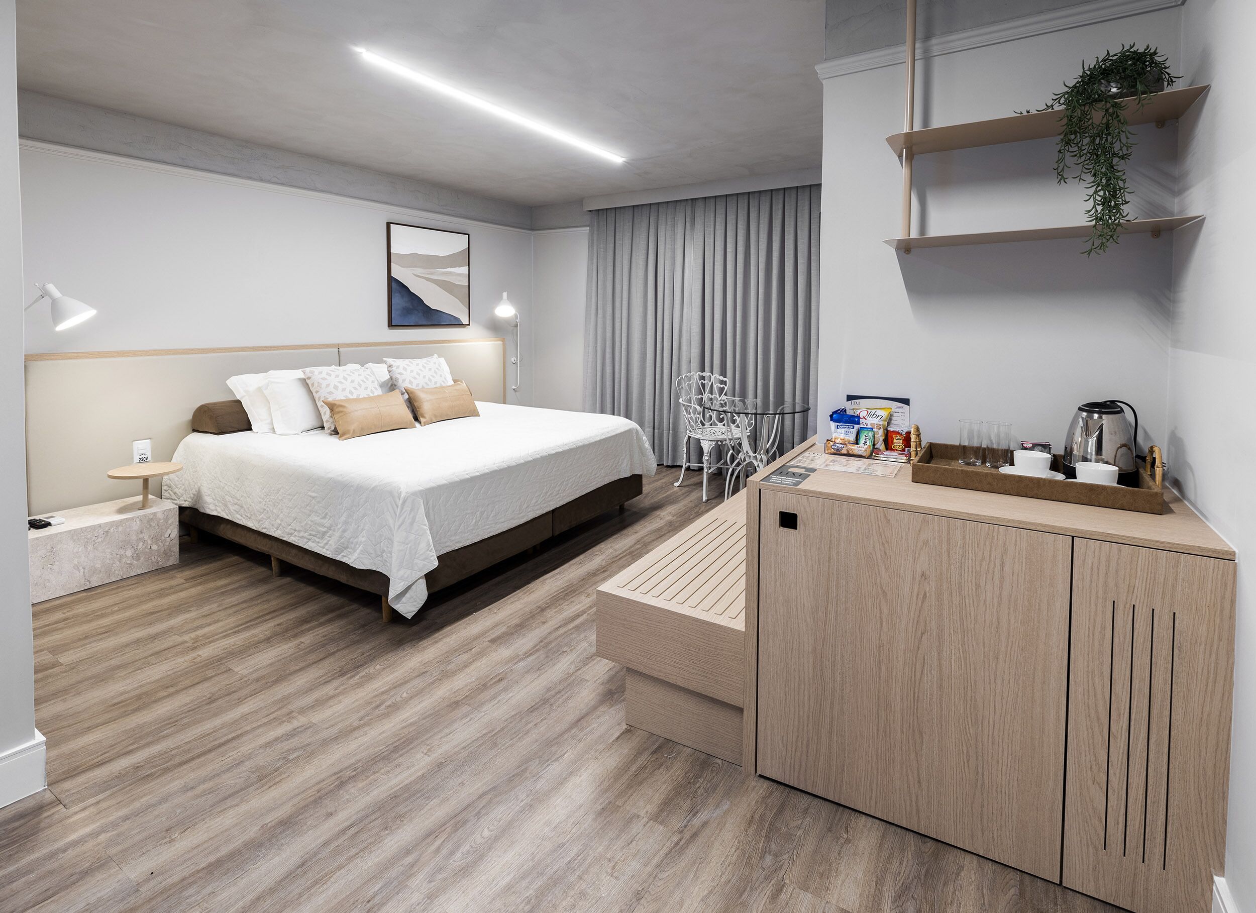 Een moderne hotelkamer met een bed, nachtkastje, lamp en een houten kast met een plant.