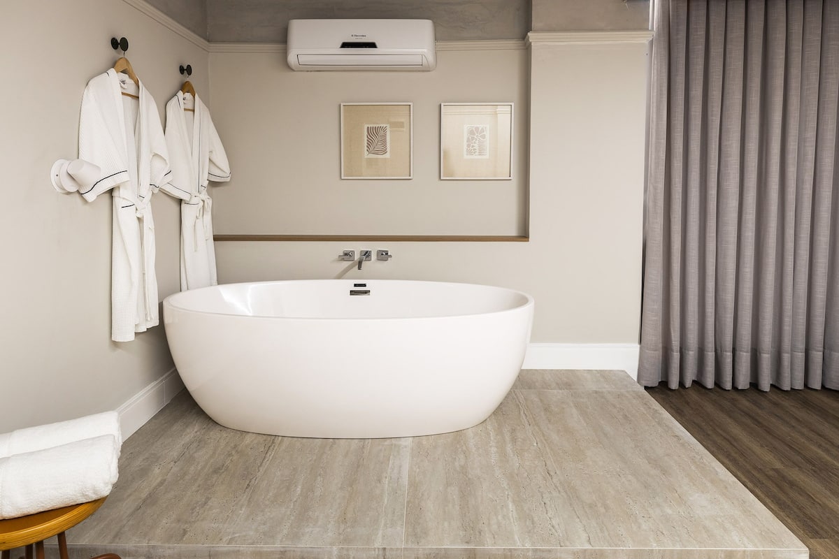 Une salle de bain moderne avec une baignoire sur pieds, deux œuvres d’art encadrées accrochées au mur et une paire de peignoirs blancs suspendus à un porte-serviettes.