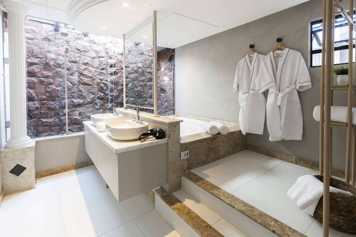 Une salle de bain moderne avec un mur en pierre, deux vasques, une baignoire et un espace douche.