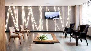 Un interior moderno con un televisor de pantalla plana montado en una pared con textura, una mesa de centro de madera con una planta y dos tipos de sillas.
