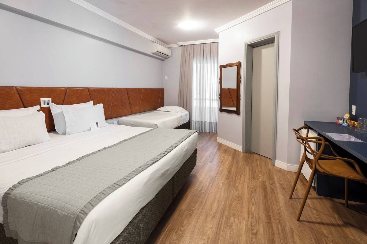 Une chambre d’hôtel avec deux lits, un bureau, une chaise, un miroir et une porte.