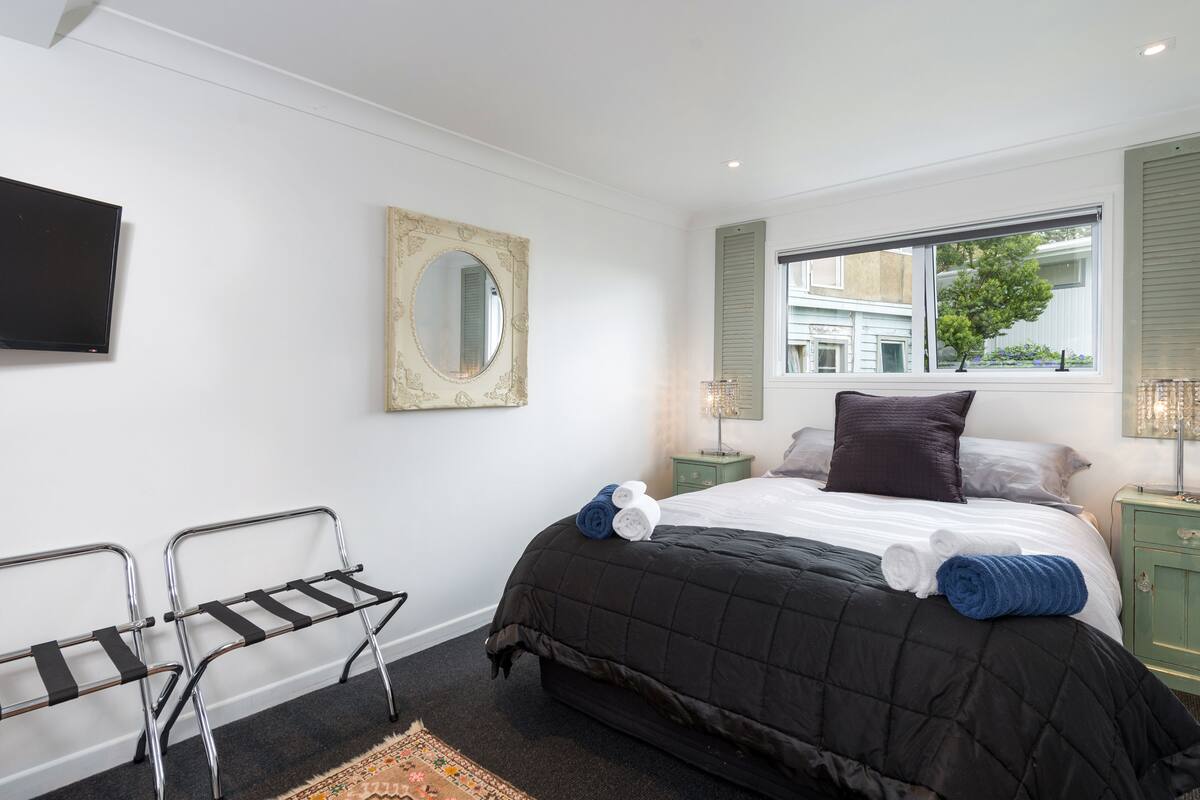 A bedroom with a bed, two nightstands, a TV, a mirror, and a window with shutters.