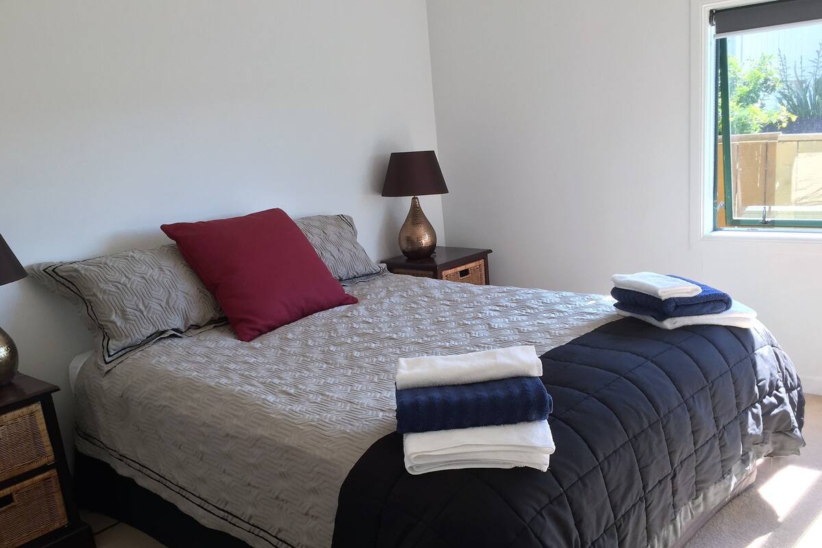 A neatly made bed with patterned bedding, a red pillow, and folded towels on the bed.