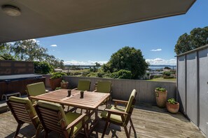 A wooden deck with a table and chairs, a barbecue grill, and potted plants. - Lakeside City Apartments (Rotorua)