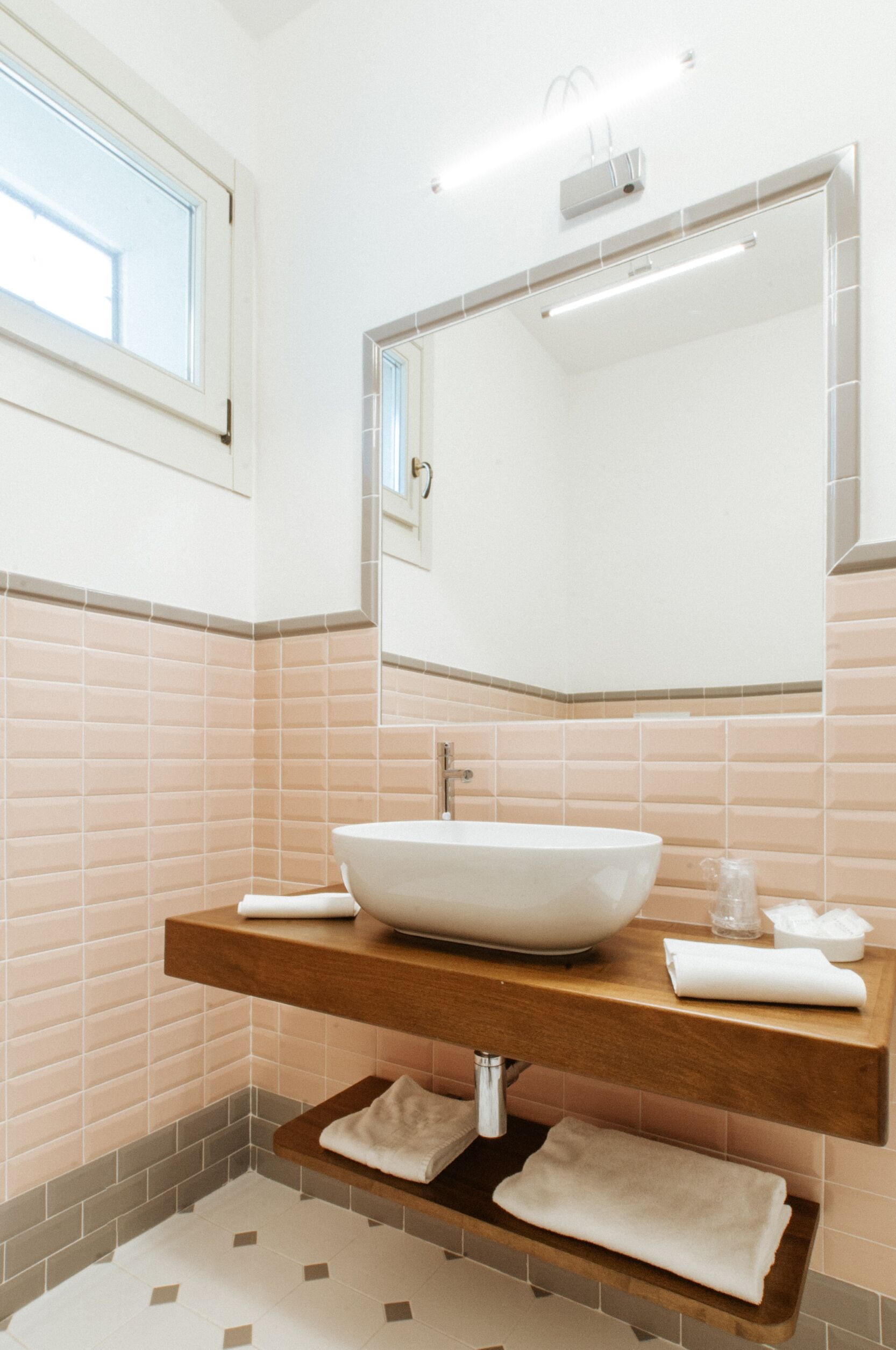 Ein modernes Badezimmer mit einem großen Spiegel, einem weißen Waschbecken auf einer Holzauslage und einem gefliesten Boden.