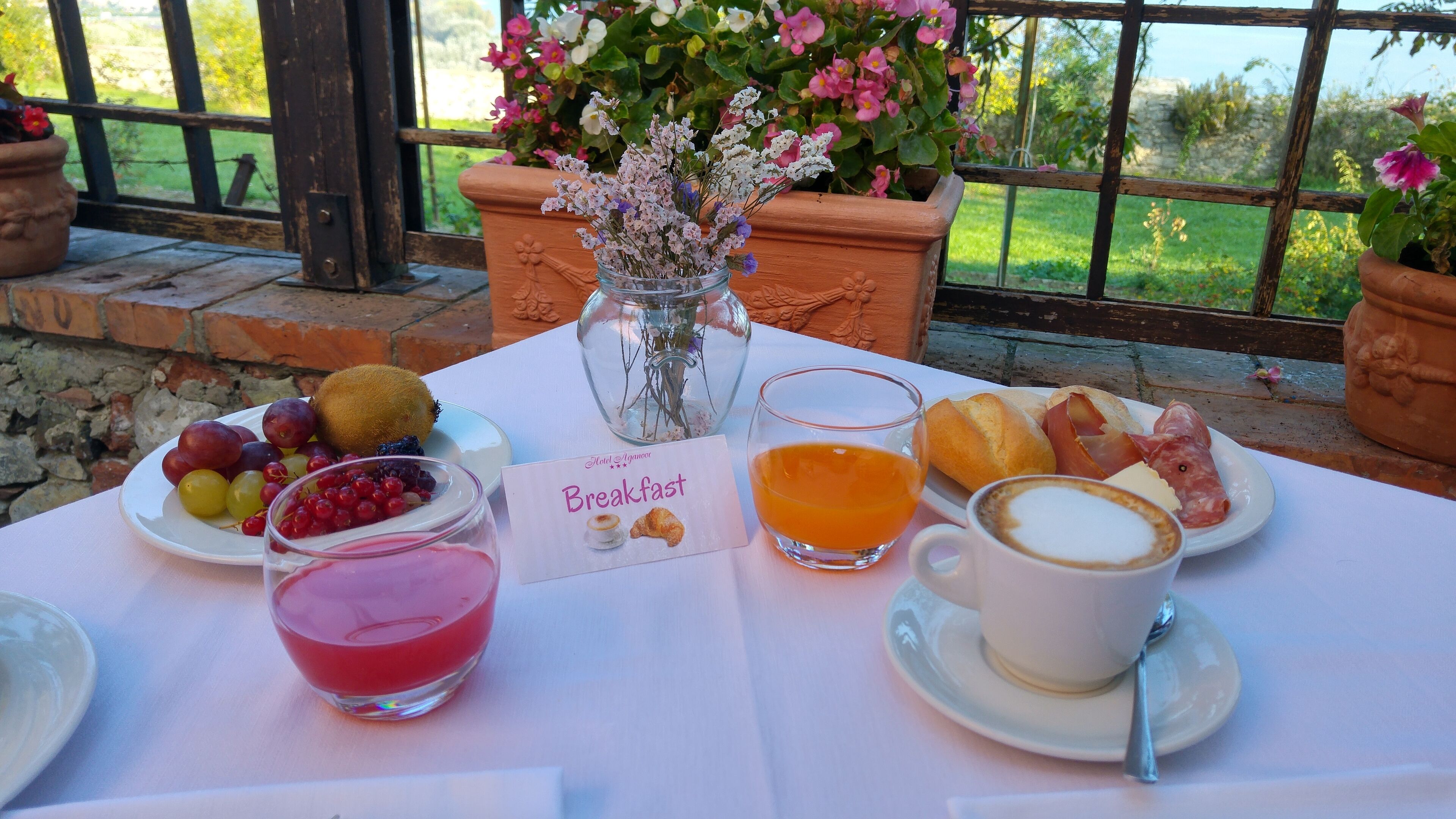 Une table de petit-déjeuner avec une variété de fruits, un verre de jus d’orange, une tasse de café et une assiette de viennoiseries.