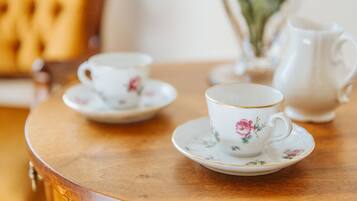 Une table ronde en bois, sur laquelle sont posées deux tasses blanches ornées de motifs floraux, ainsi qu’une théière assortie.