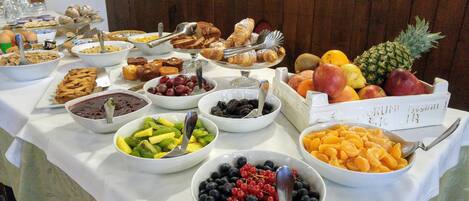 Una mesa de buffet con diversos alimentos, entre ellos frutas, pasteles y postres.