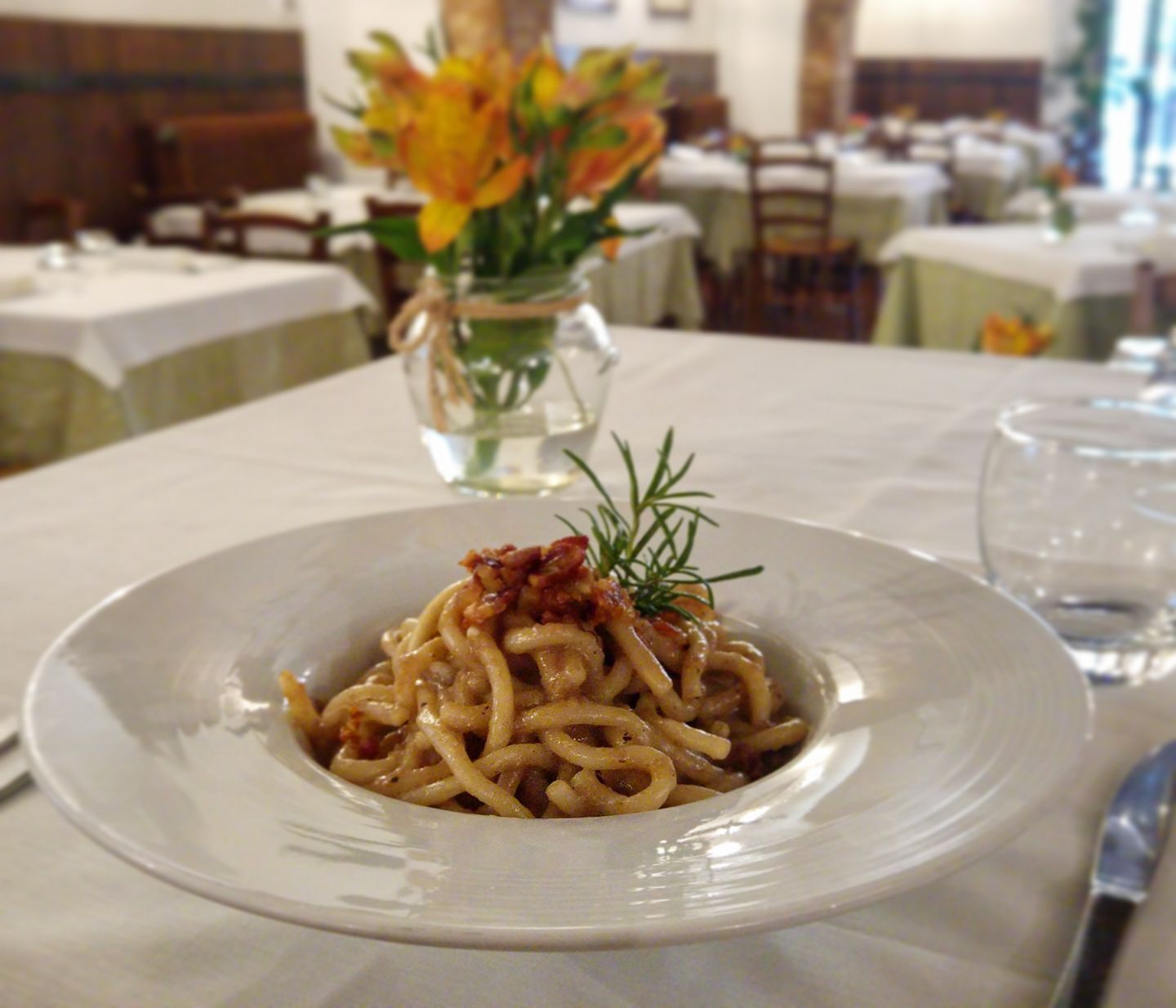 Un plato de espagueti con decoración, sobre una mesa en un comedor con otras mesas y sillas al fondo.