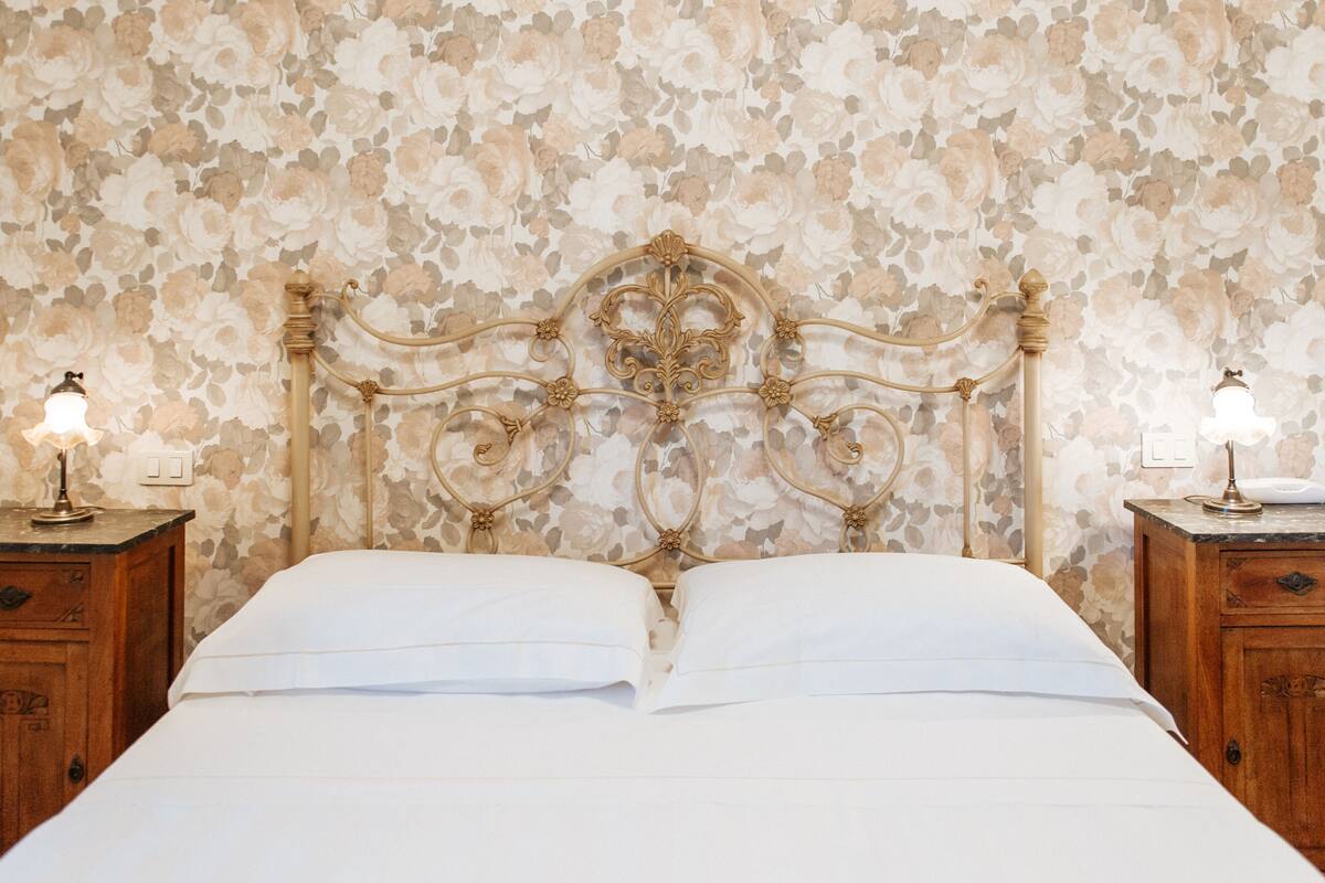 Un lit avec un mur recouvert d’un papier peint à motifs floraux, une tête de lit en bois et des lampes de chevet.