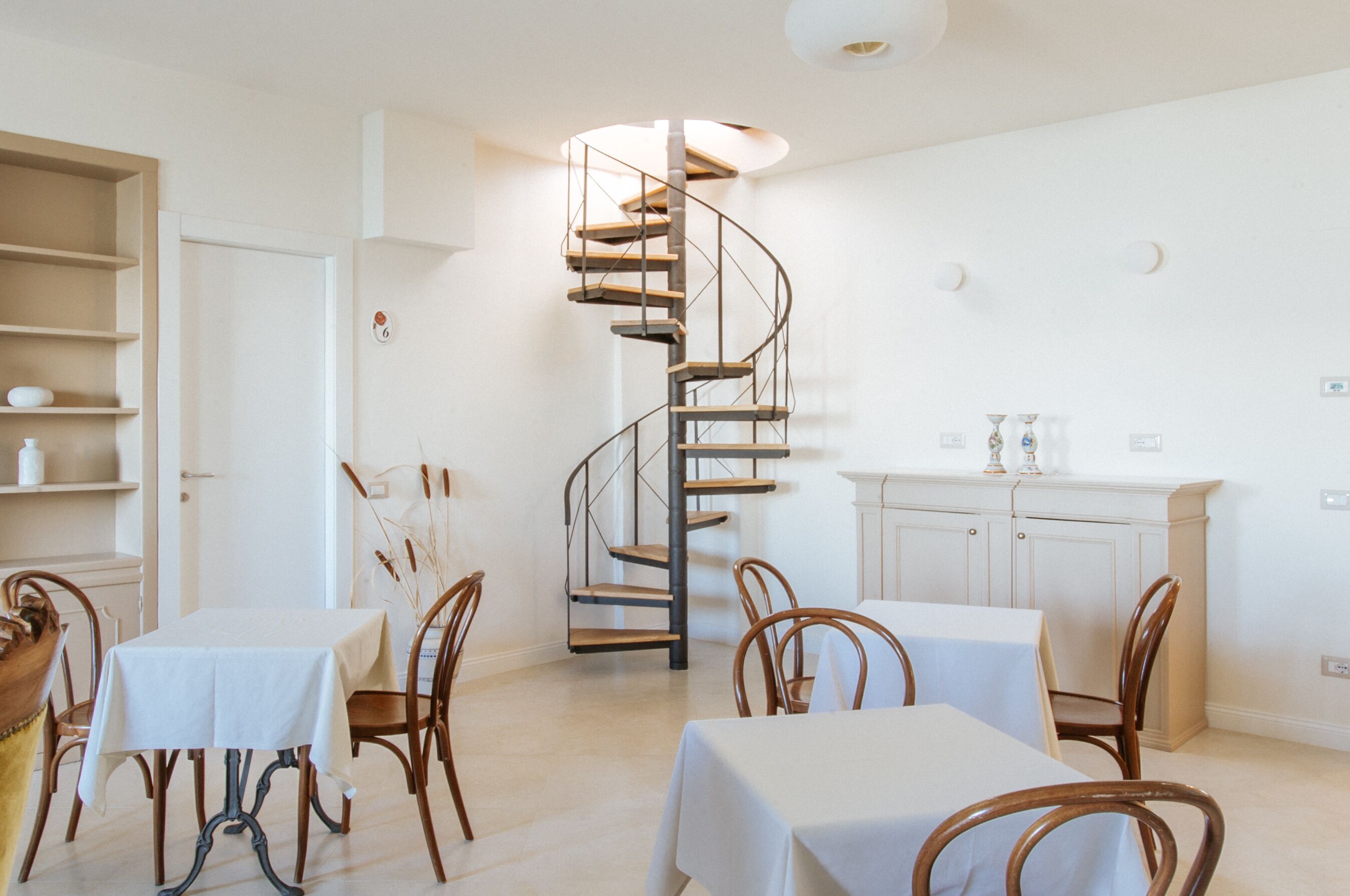 A dining area with a spiral staircase, white walls, and wooden furniture.