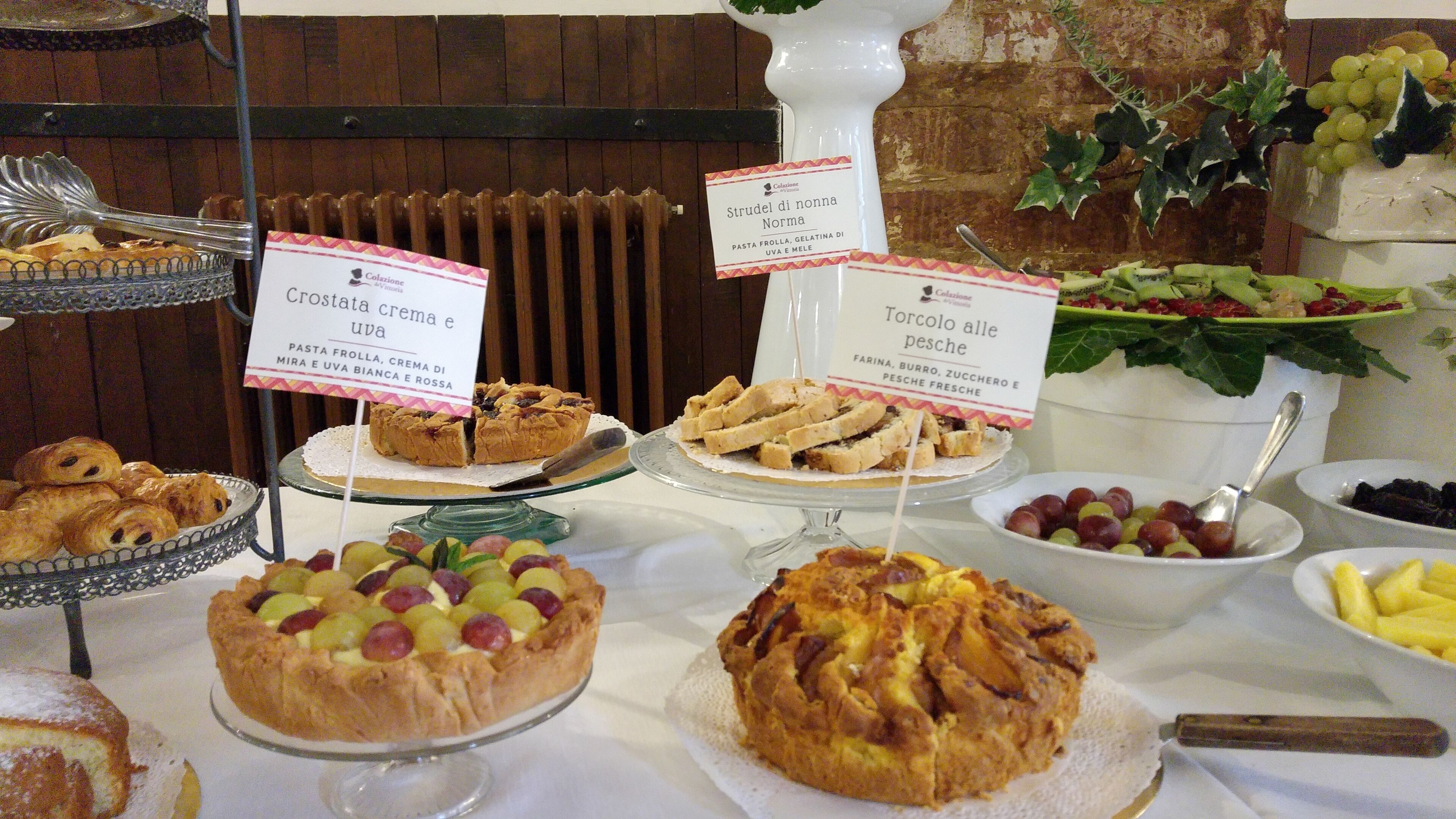 Un bufé con diversos platos, incluyendo crostata crema e uva, torcolo alle pesche y otros postres.