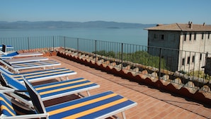 Une terrasse avec des chaises longues donnant sur une étendue d’eau et un bâtiment en pierre.