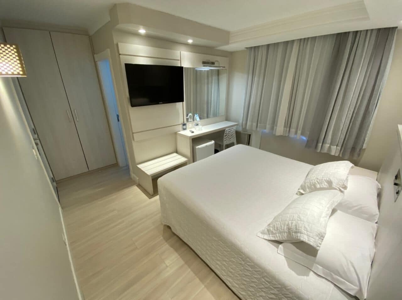 Une chambre d’hôtel moderne dotée d’un grand lit, d’un téléviseur fixé au mur, d’une coiffeuse avec un miroir et d’un dressing.