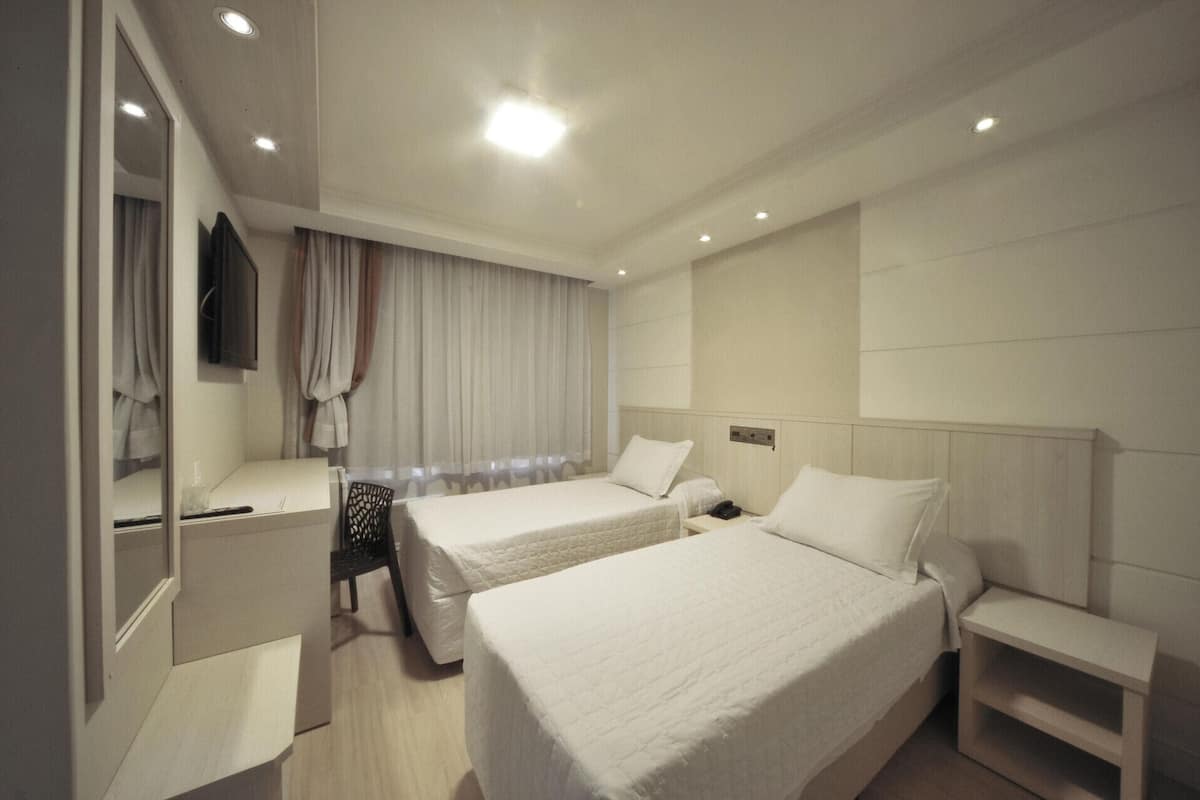 Habitación de hotel con dos camas, un escritorio, una silla, un televisor y una ventana con cortinas.