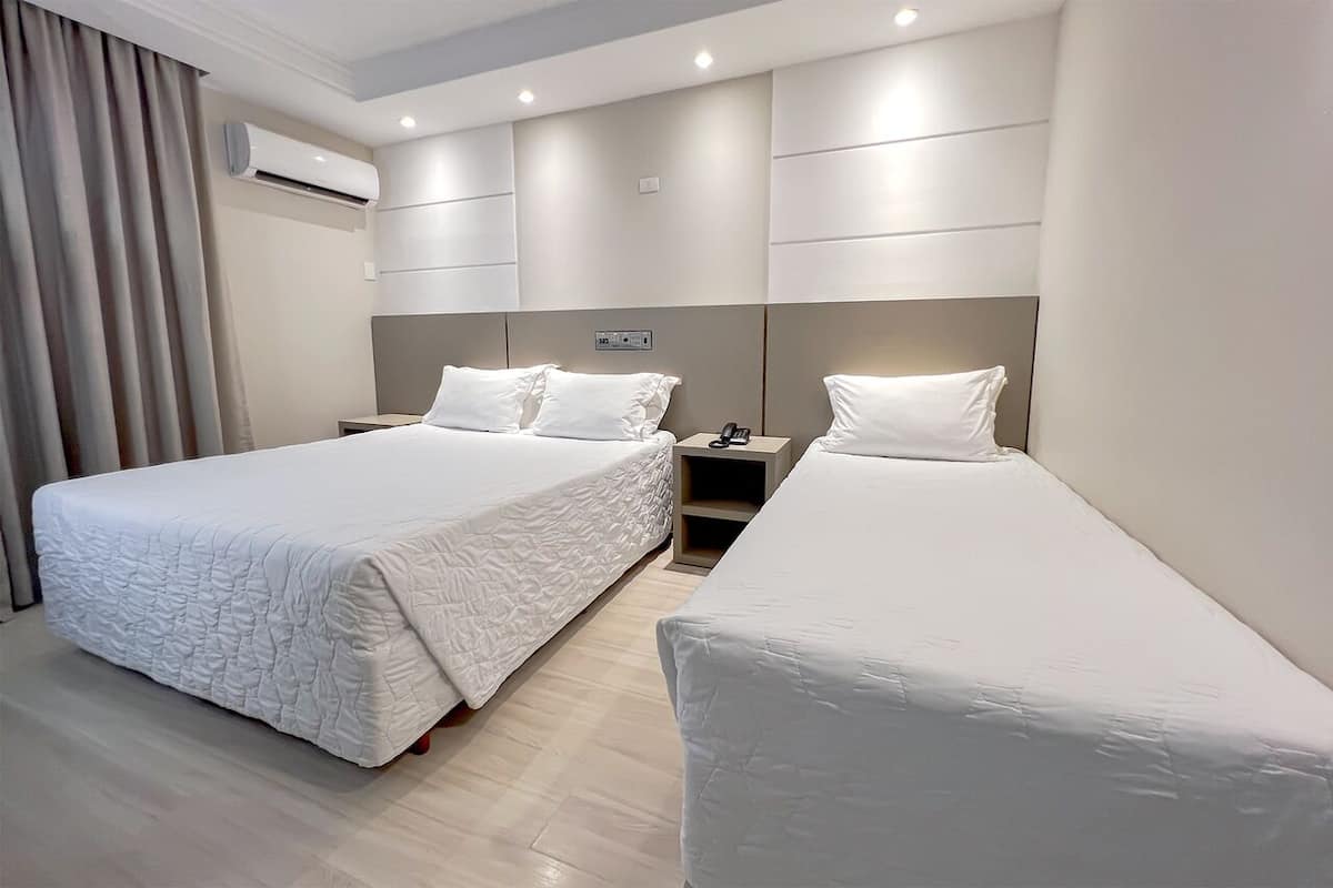 A modern hotel room with two beds, a bedside table, a nightstand, and an air conditioning unit.