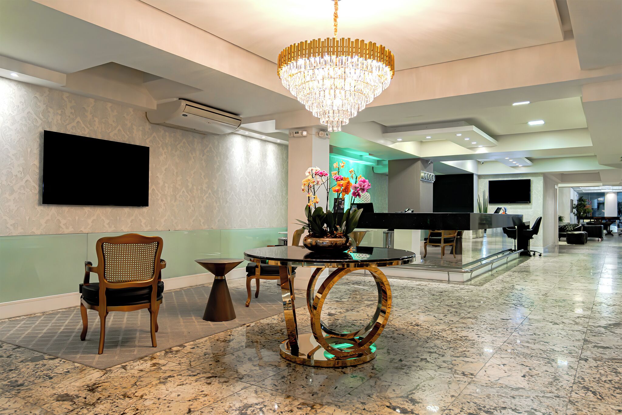 Um saguão com um candelabro, um balcão de recepção, uma TV de tela plana e uma área de estar com uma mesa e cadeiras.