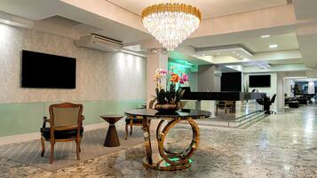Um saguão com um candelabro, um balcão de recepção, uma TV de tela plana e uma área de estar com uma mesa e cadeiras.