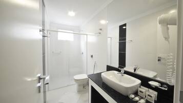 Ein modernes Badezimmer mit Duschkabine aus Glas, einer weißen Toilette, einer schwarzen Ablagefläche mit Waschbecken und einem an der Wand befestigten Föhn.