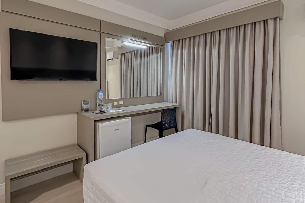 A hotel room with a bed, a desk with a computer, a television, and a mirror.