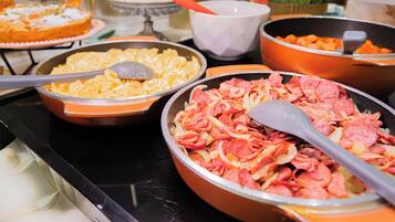 A buffet table with various dishes, including a large bowl of sliced meat and a bowl of scrambled eggs.