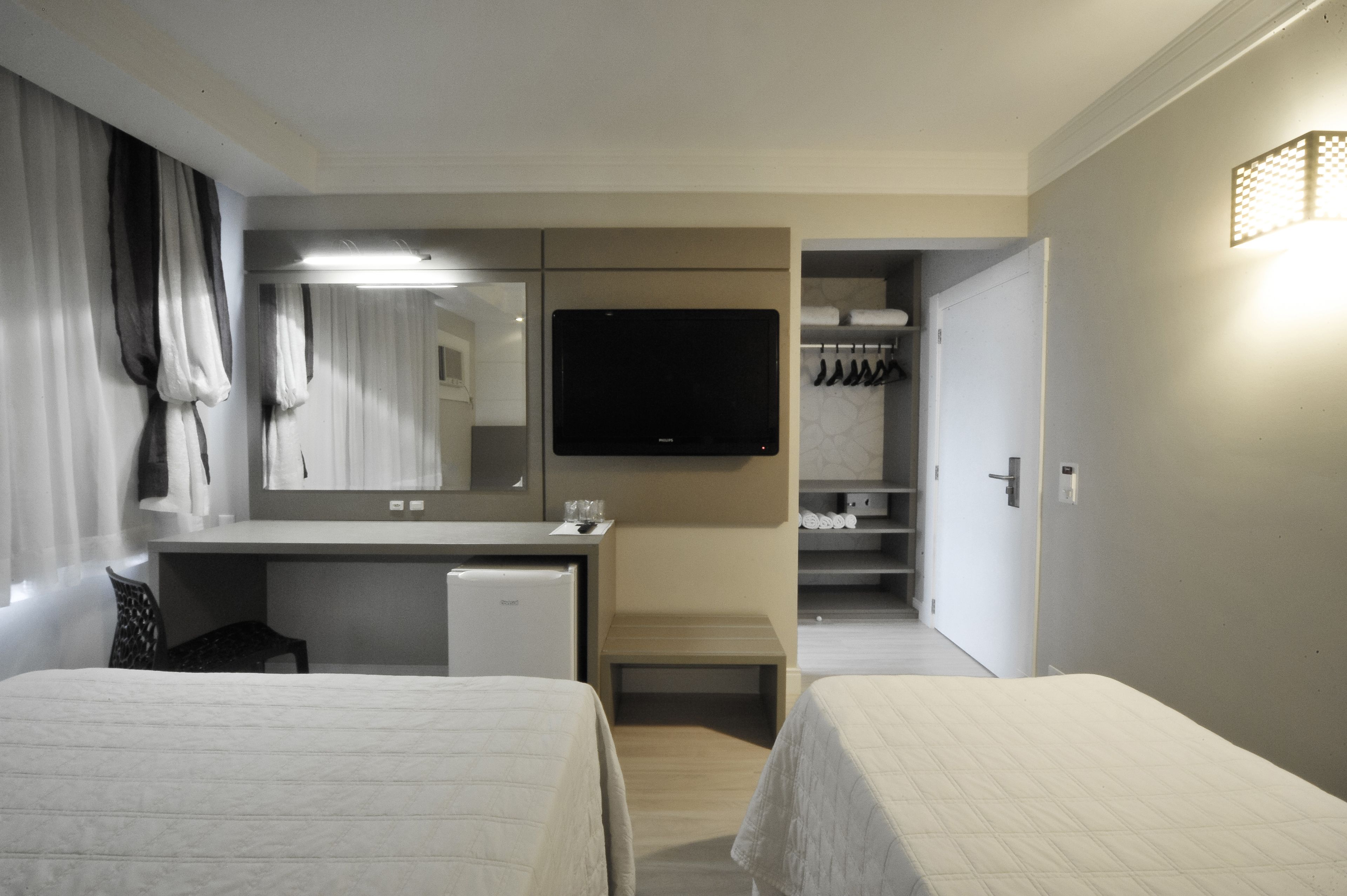 A hotel room with two beds, a desk, a television, a mini-fridge, and a walk-in closet.