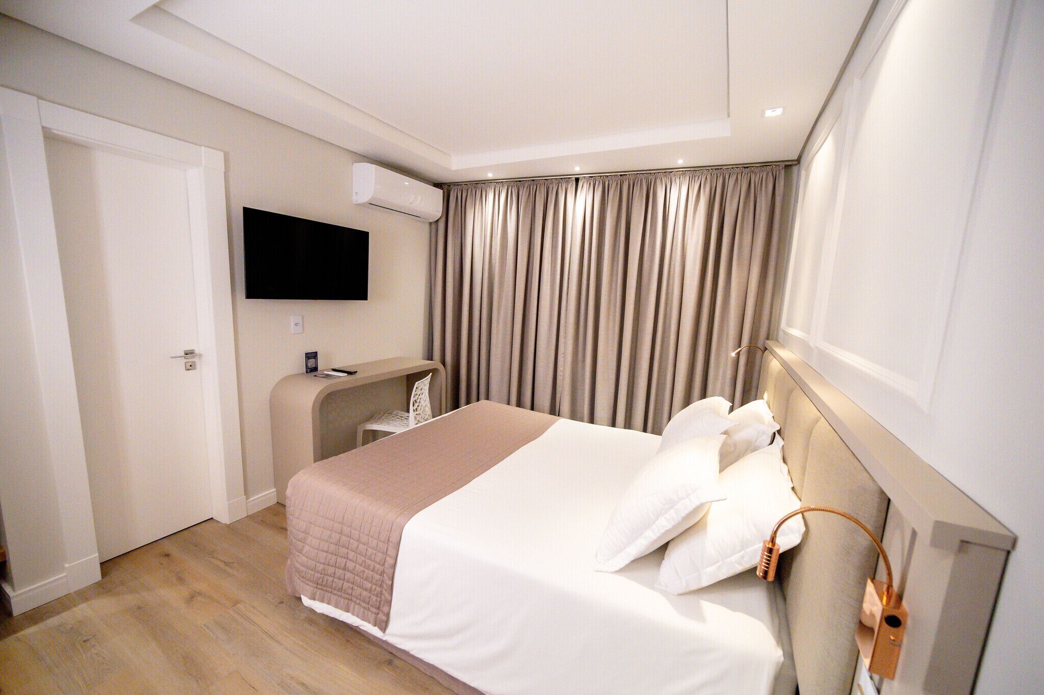 A hotel room with a bed, a desk, a TV, and a curtain.