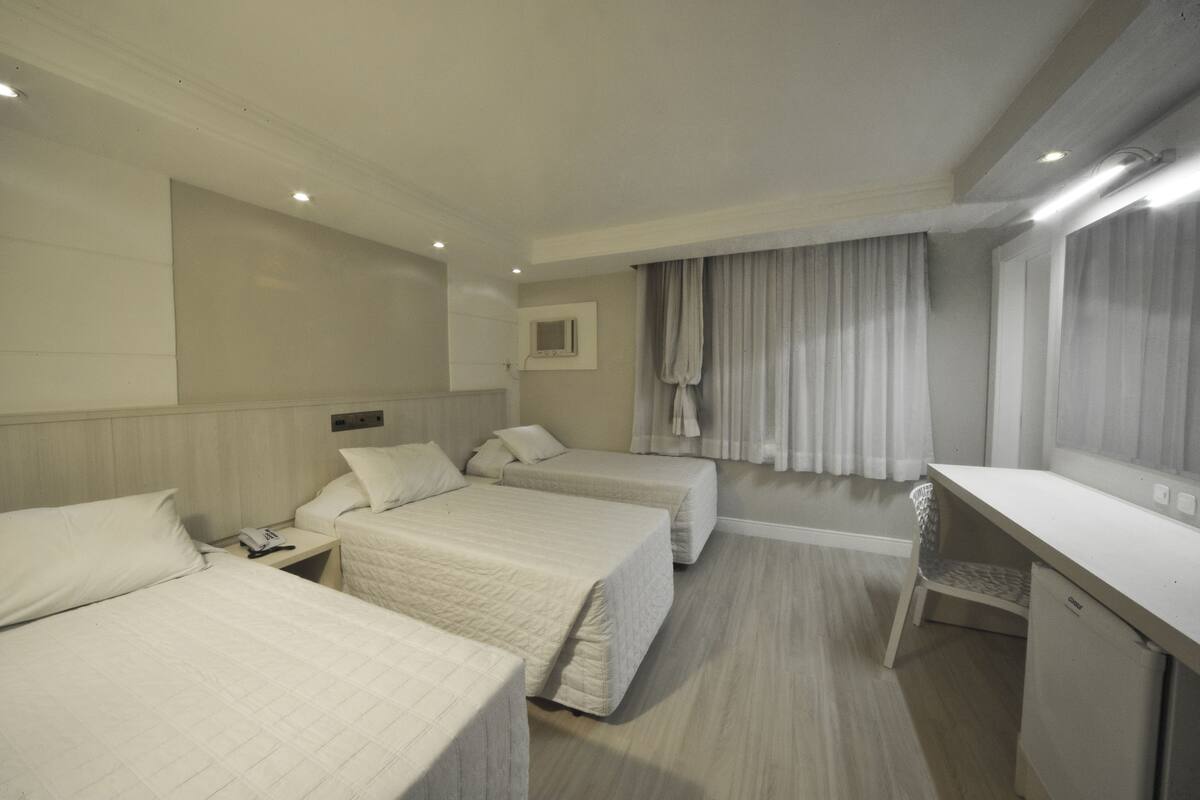 A hotel room with two beds, a desk, a chair, a television, and a window with curtains.