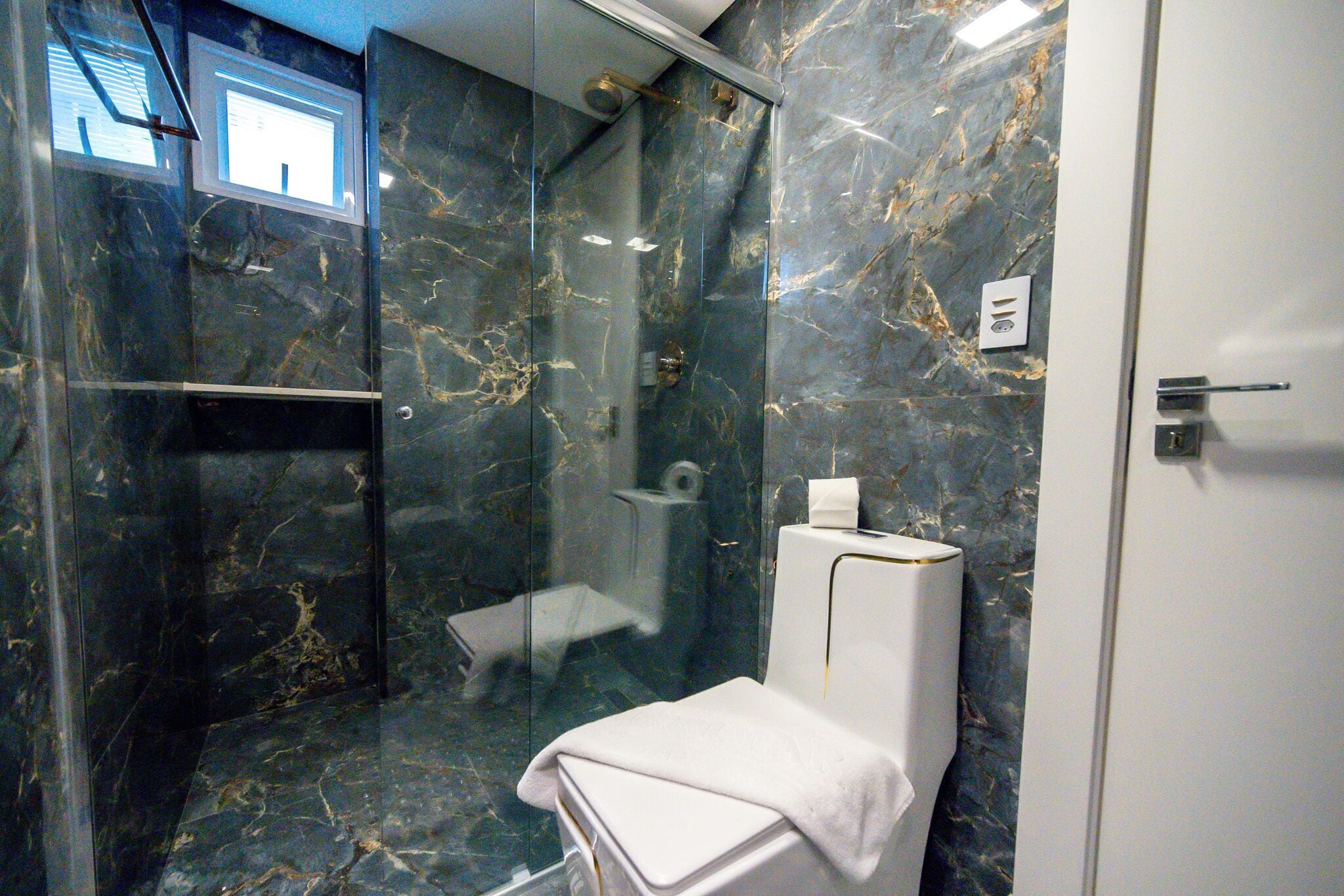 Un baño con ducha de vidrio, paredes de mármol, inodoro y perchero.
