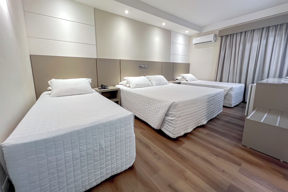 A hotel room with three single beds, a desk, and a wardrobe.