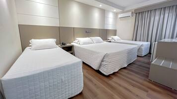 A hotel room with three single beds, a desk, and a wardrobe.