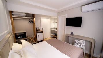 Quarto de hotel com cama, escrivaninha, televisão, guarda-roupa e espelho.