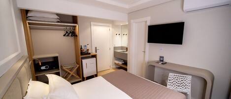 A hotel room with a bed, a desk, a TV, a wardrobe, and a mirror.