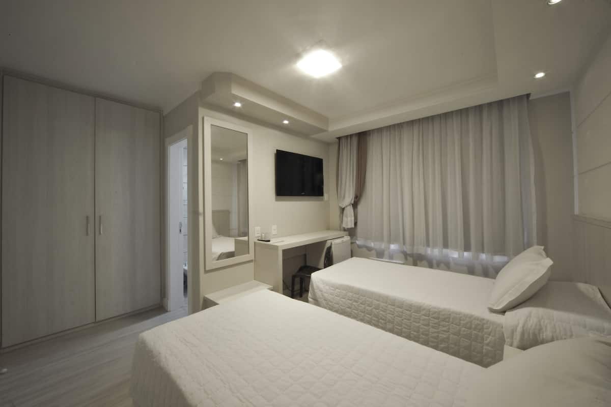 A hotel room with a bed, a desk, a mirror, and a wardrobe.