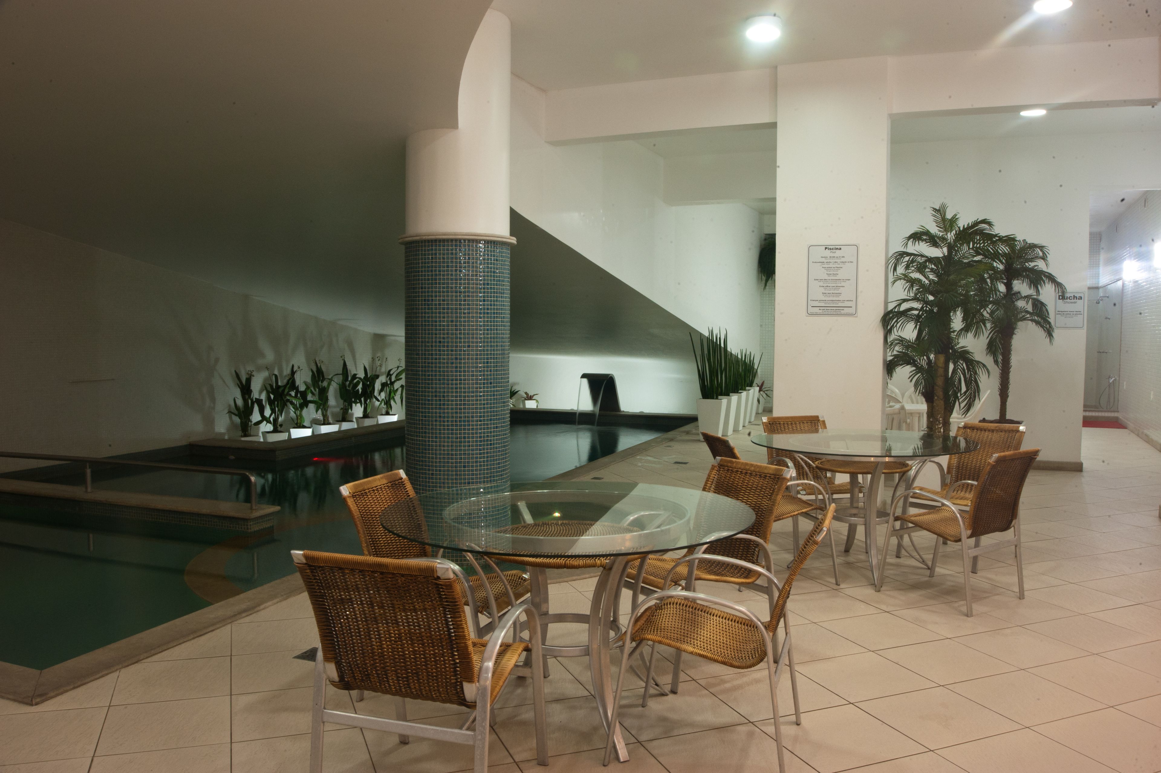 Un espace piscine agrémenté d’une table en verre et de chaises en osier, entouré de plantes en pot et doté d’un sol carrelé.
