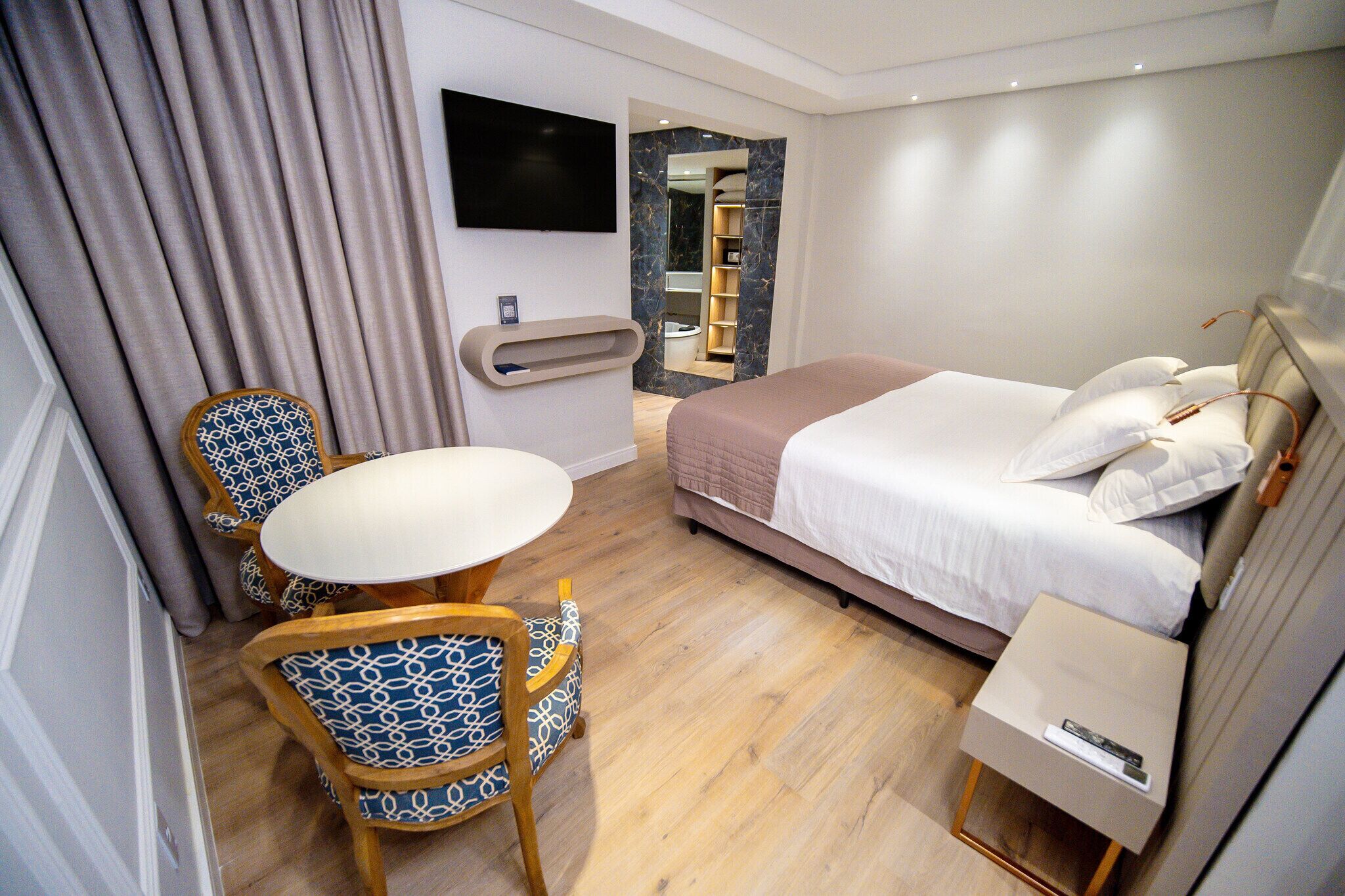 Camera d'albergo con letto, comodino, televisore e una zona salotto con tavolo e sedie.