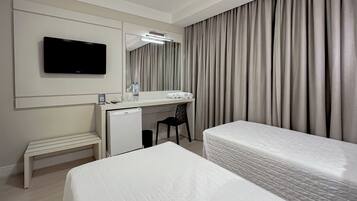 A hotel room with a bed, a desk with a computer, a television, and a large window with curtains.